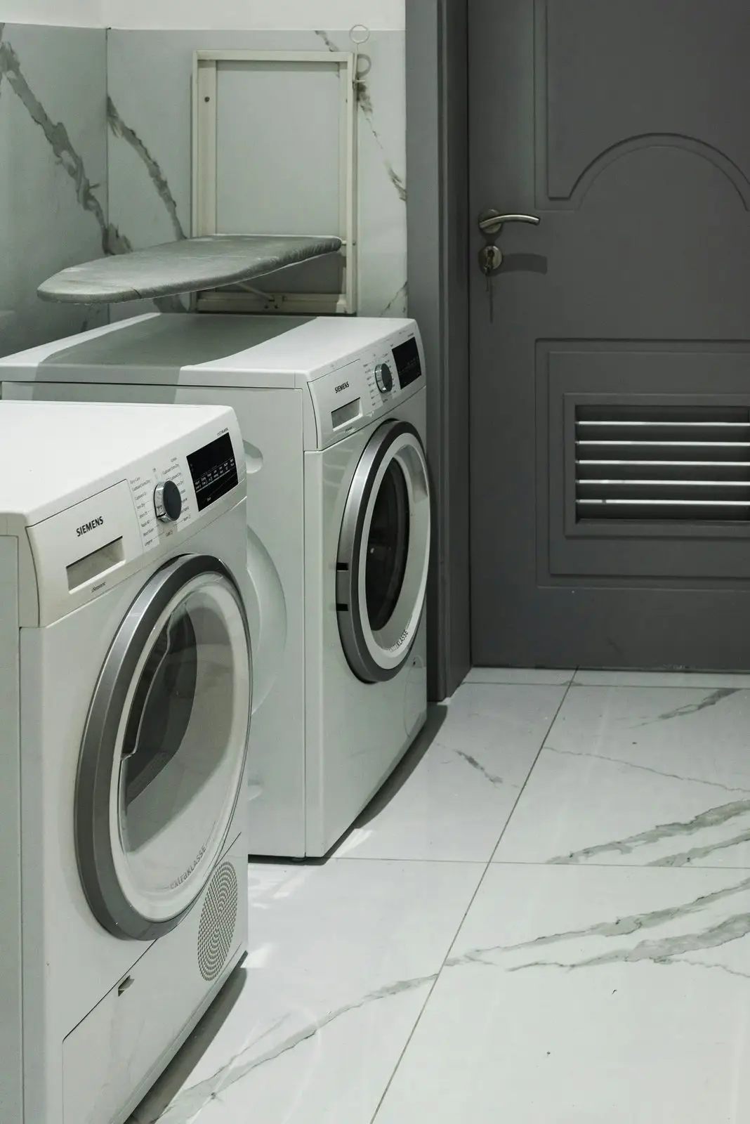 A laundry with a marble-look tiled splashback and side-by-side washer and dryer