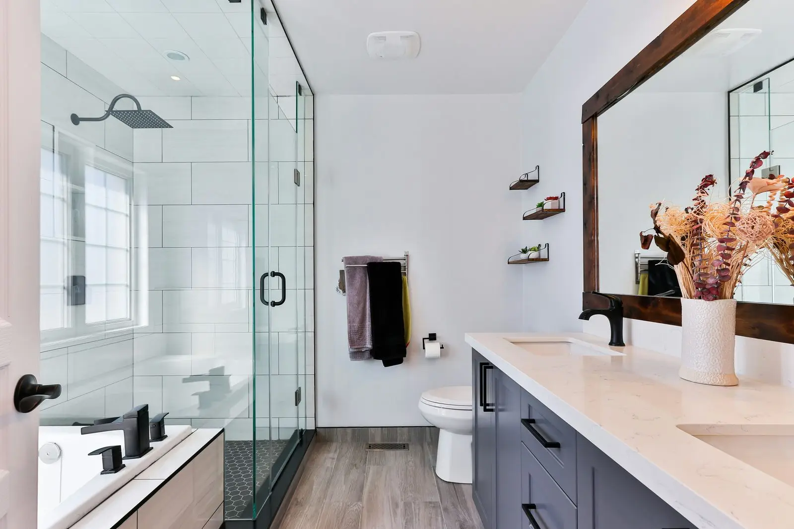 A white-tiled bathroom with a frameless glass shower screen and black tapware