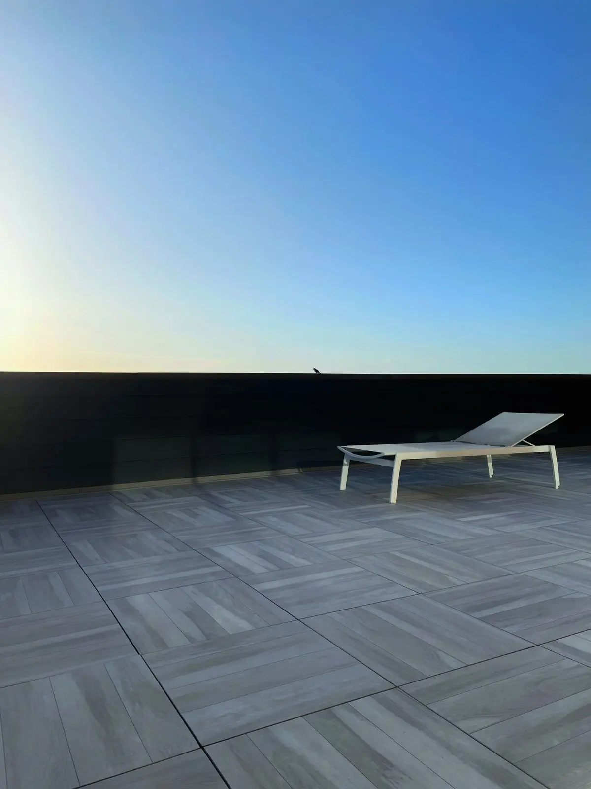 A tiled rooftop terrace at dusk with a sun lounger against an open horizon