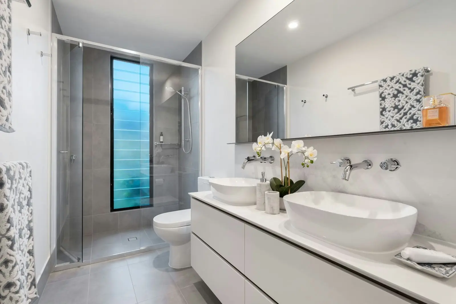 A bathroom with twin basins on a wall-hung vanity and a glass walk-in shower